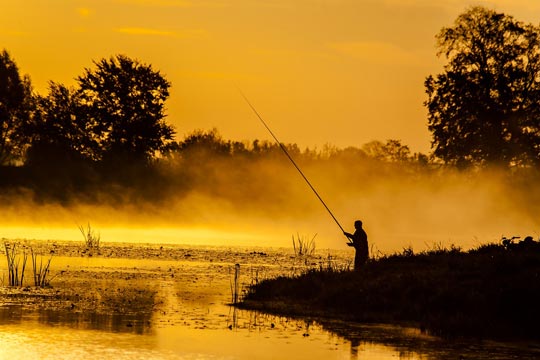Un pescador pescando al amanecer en un río