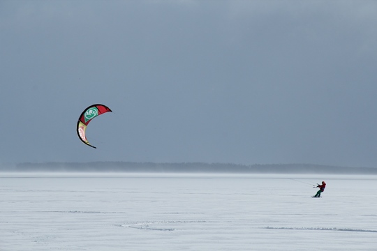 Un deportista solitario practicando snowkiting sobre un lago congelado un día con sol de invierno