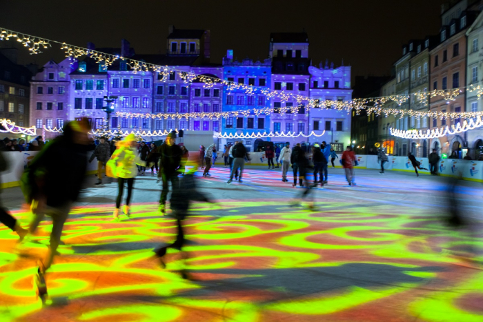 Foto realizzata nella Città Vecchia di Varsavia. Mostra la piazza illuminata da luci Natalizie, e delle persone che pattinano sul ghiaccio al centro della piazza